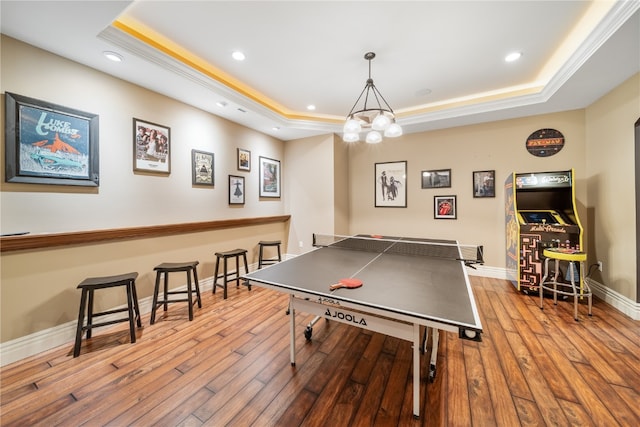 recreation room featuring a notable chandelier, light hardwood / wood-style floors, and a raised ceiling