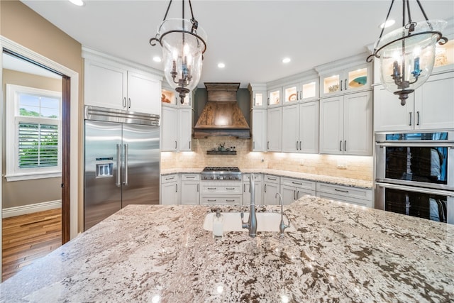 kitchen featuring sink, white cabinetry, custom range hood, appliances with stainless steel finishes, and hardwood / wood-style floors