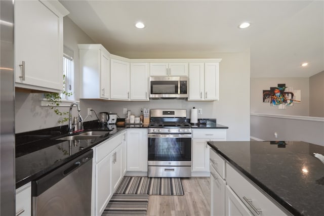 kitchen with appliances with stainless steel finishes, dark stone countertops, white cabinetry, light wood-type flooring, and sink