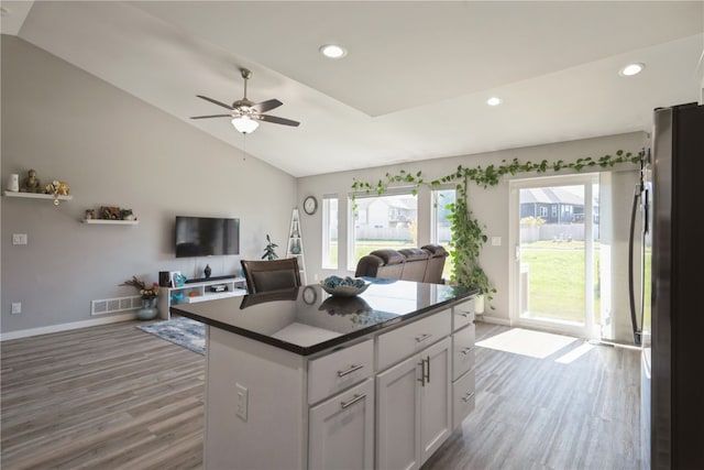 kitchen with stainless steel fridge, white cabinetry, vaulted ceiling, wood-type flooring, and ceiling fan