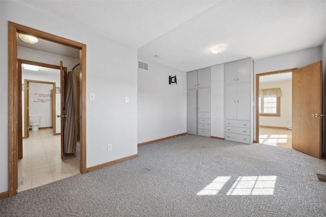 unfurnished bedroom with light carpet, a closet, ensuite bath, and a textured ceiling