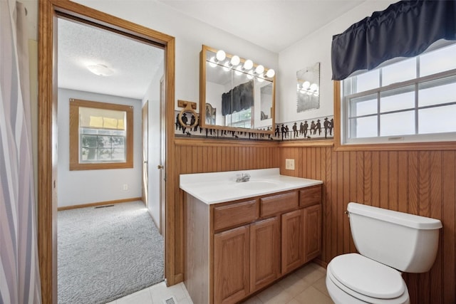 bathroom with a textured ceiling, a healthy amount of sunlight, vanity, and toilet