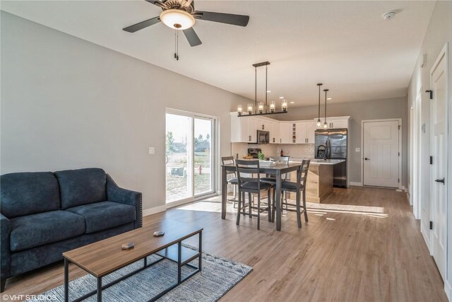 living room with light wood-type flooring and ceiling fan with notable chandelier