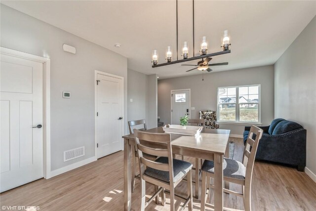 dining space with ceiling fan with notable chandelier and light wood-type flooring