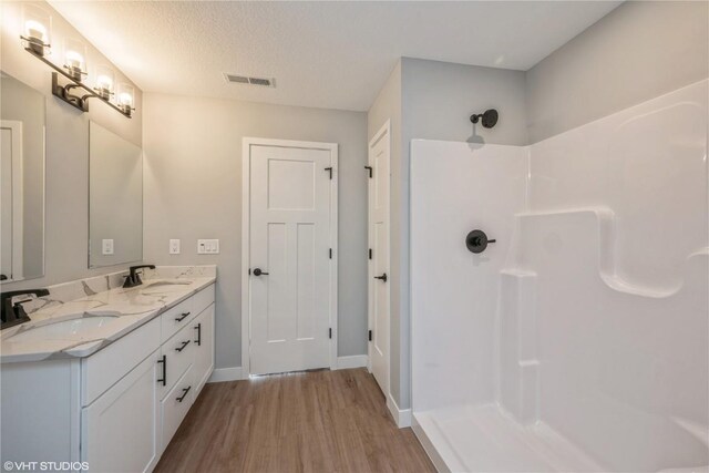 bathroom with hardwood / wood-style floors, vanity, a textured ceiling, and walk in shower