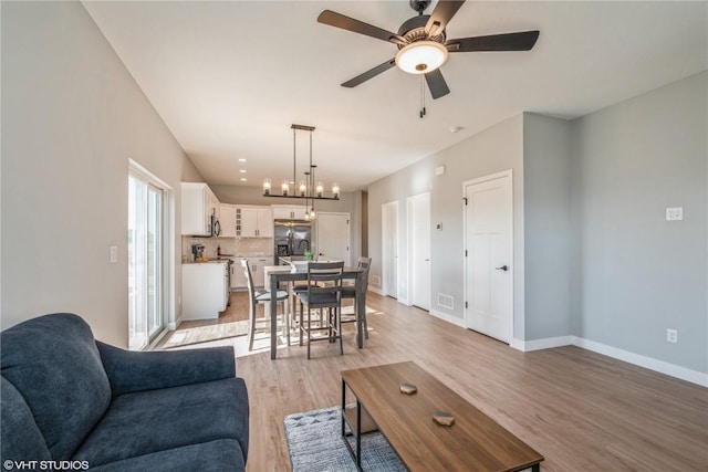 living room featuring ceiling fan with notable chandelier and light hardwood / wood-style flooring