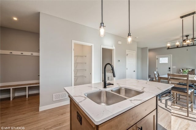 kitchen with pendant lighting, sink, light stone countertops, an island with sink, and light hardwood / wood-style floors