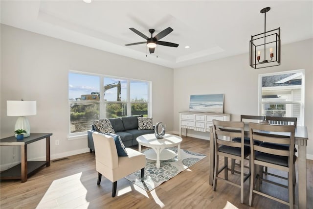 living room with ceiling fan with notable chandelier, light wood-type flooring, and a tray ceiling