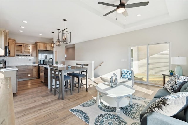 living room with a raised ceiling, ceiling fan with notable chandelier, and light hardwood / wood-style flooring