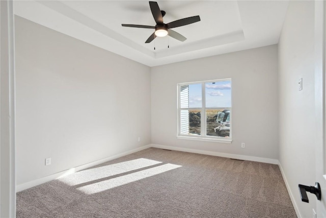 carpeted empty room with a raised ceiling and ceiling fan