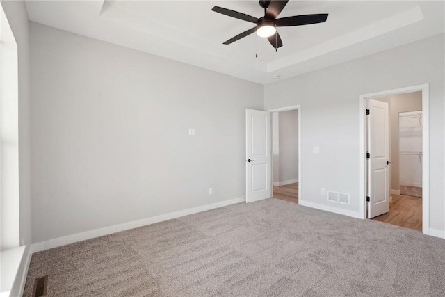 unfurnished bedroom featuring a walk in closet, light colored carpet, ceiling fan, and a tray ceiling