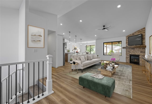 living room with ceiling fan, light wood-type flooring, sink, a fireplace, and vaulted ceiling