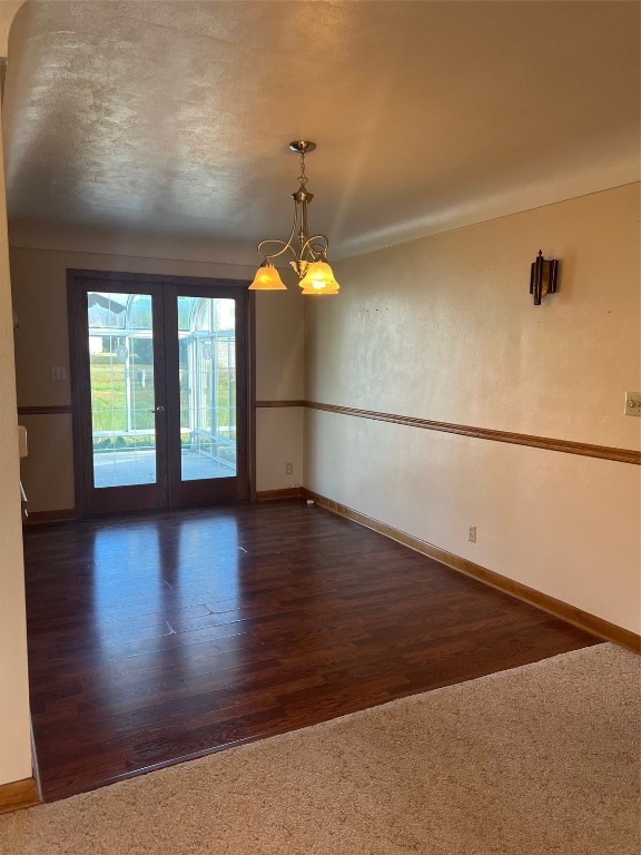 unfurnished room featuring a textured ceiling, a chandelier, and dark wood-type flooring