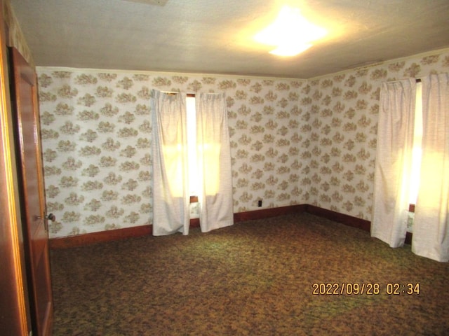 empty room with dark colored carpet and a textured ceiling