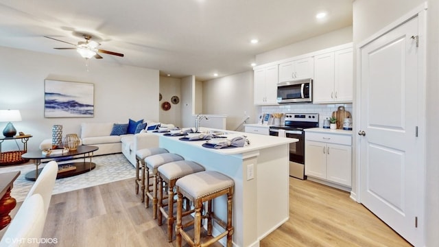 kitchen featuring an island with sink, stainless steel appliances, white cabinetry, and light hardwood / wood-style flooring