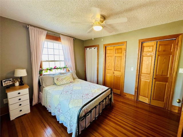 bedroom with dark wood-type flooring, ceiling fan, a textured ceiling, and two closets