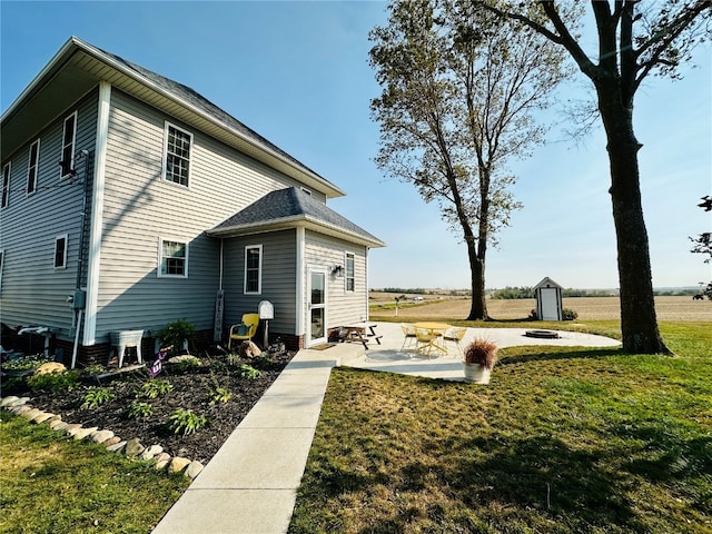 rear view of house with a shed, a patio area, and a lawn