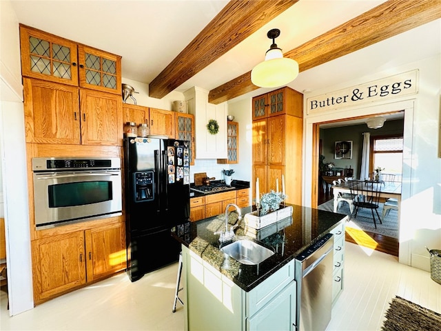 kitchen with beamed ceiling, stainless steel appliances, a center island with sink, sink, and pendant lighting