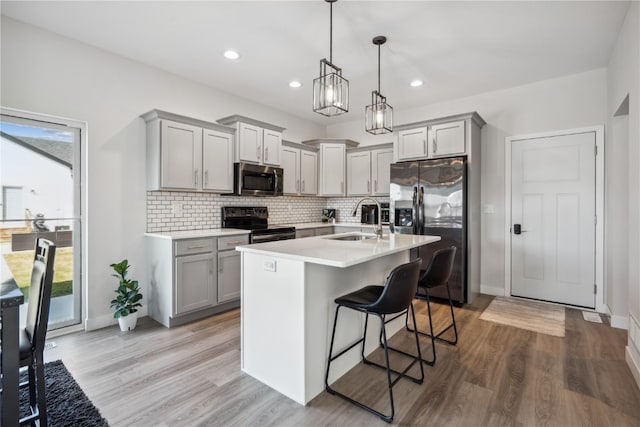 kitchen with pendant lighting, sink, hardwood / wood-style flooring, appliances with stainless steel finishes, and a kitchen bar