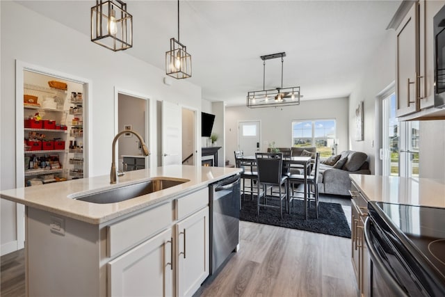 kitchen with pendant lighting, a kitchen island with sink, sink, white cabinets, and black appliances