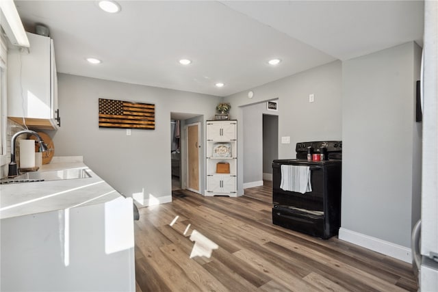 kitchen featuring hardwood / wood-style flooring, black range with electric cooktop, sink, and white cabinets