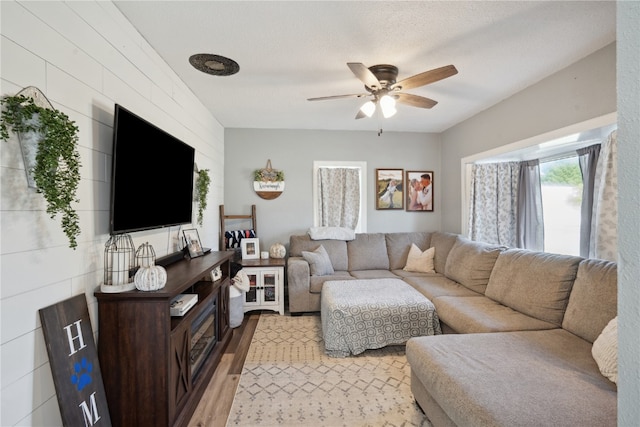 living room featuring light wood-type flooring, a textured ceiling, and ceiling fan