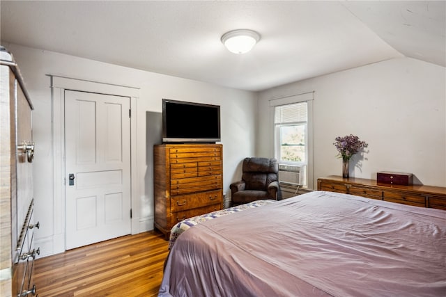 bedroom with cooling unit, lofted ceiling, and light hardwood / wood-style floors