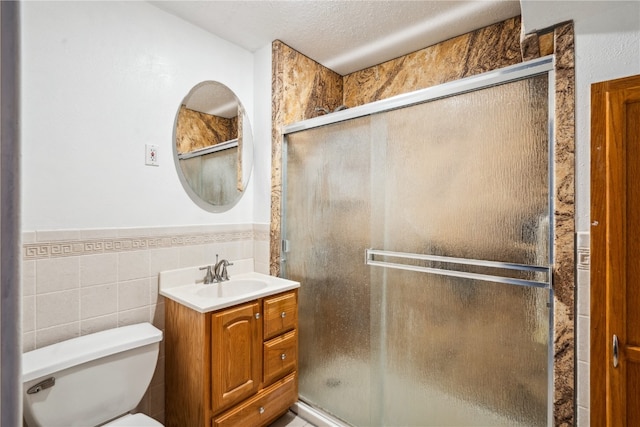 bathroom featuring tile walls, a textured ceiling, a shower with door, vanity, and toilet