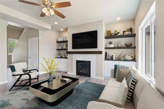 living room featuring a glass covered fireplace, baseboards, recessed lighting, and wood finished floors