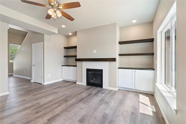 unfurnished living room featuring a glass covered fireplace, recessed lighting, wood finished floors, and baseboards