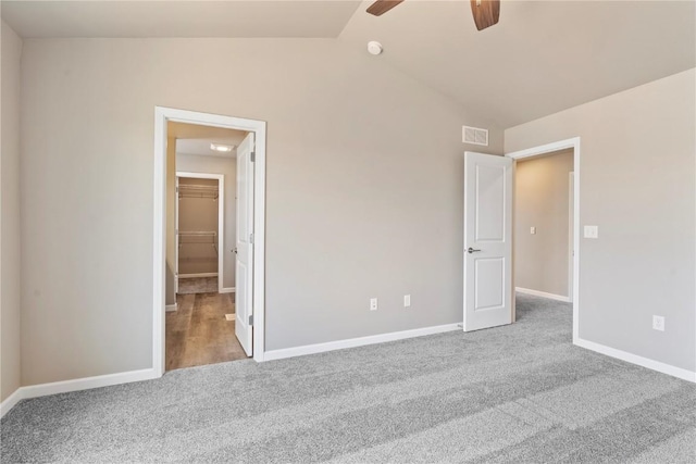 unfurnished bedroom featuring carpet floors, lofted ceiling, a walk in closet, and baseboards