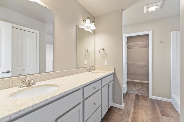 bathroom with double vanity, visible vents, a sink, wood finished floors, and baseboards