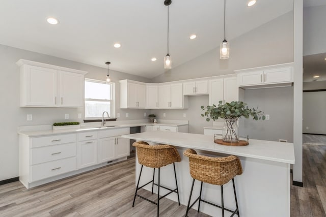 kitchen with white cabinets, pendant lighting, sink, a center island, and light hardwood / wood-style floors