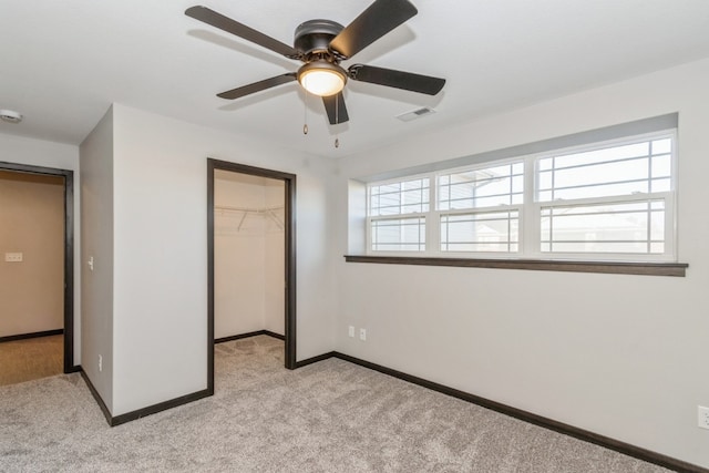 unfurnished bedroom featuring ceiling fan, light colored carpet, a closet, and a walk in closet