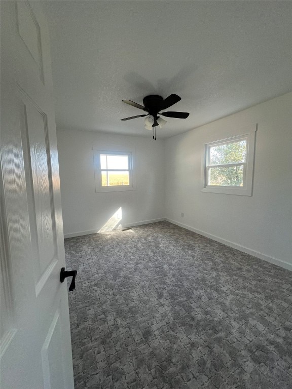 empty room featuring ceiling fan, dark carpet, and a wealth of natural light