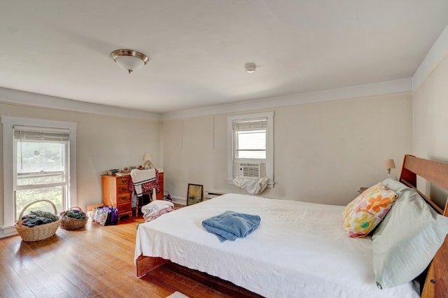 bedroom with wood-type flooring, cooling unit, and multiple windows