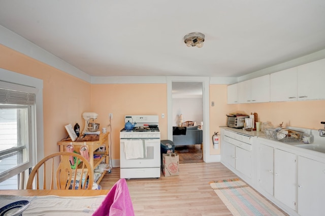 kitchen with white gas stove, sink, light hardwood / wood-style flooring, and white cabinets