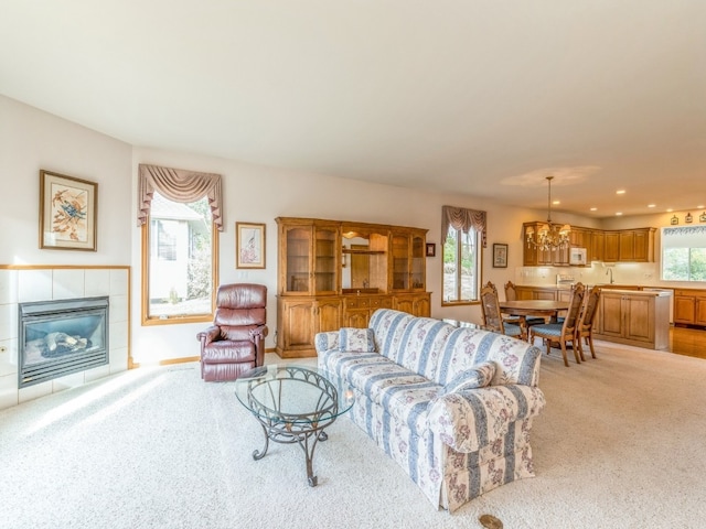 living room with a wealth of natural light, a notable chandelier, a tiled fireplace, and light colored carpet