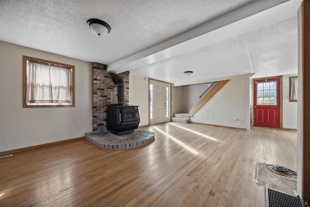 unfurnished living room with hardwood / wood-style floors, a textured ceiling, and a wood stove