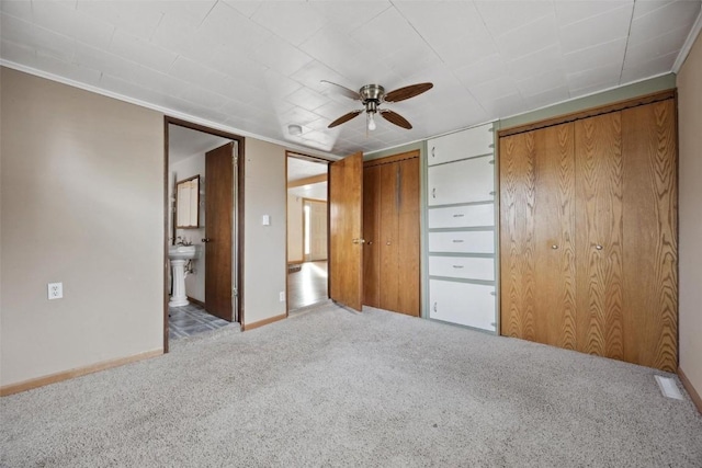 unfurnished bedroom featuring connected bathroom, light colored carpet, ceiling fan, and multiple closets