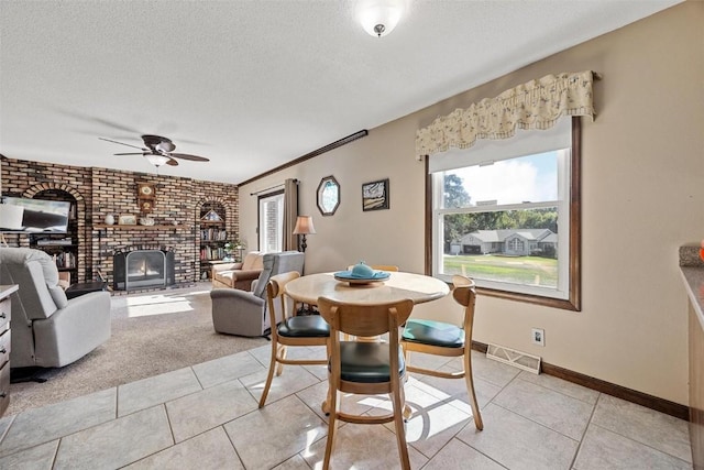 dining room with ceiling fan, a textured ceiling, a fireplace, light tile patterned floors, and ornamental molding