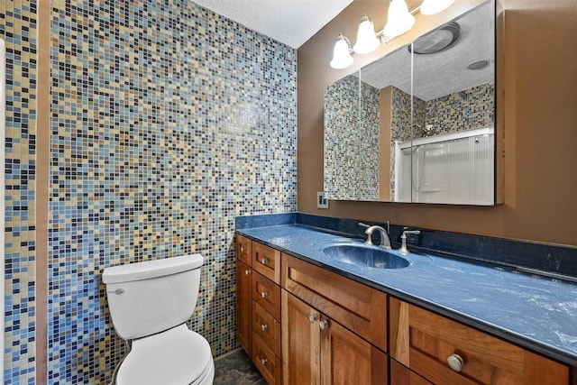 bathroom with a textured ceiling, vanity, tile walls, and toilet