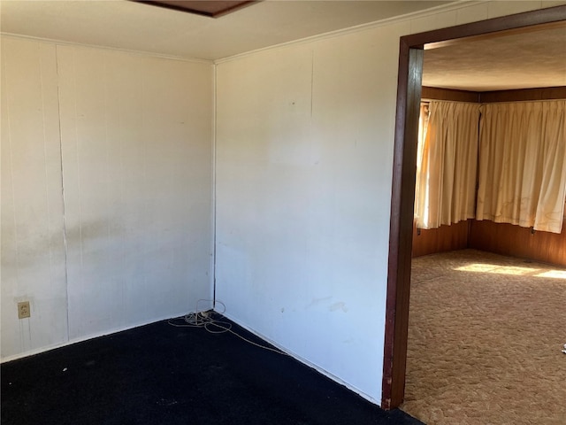 unfurnished room with crown molding, carpet flooring, and wooden walls