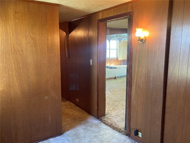 hallway featuring light carpet and wooden walls