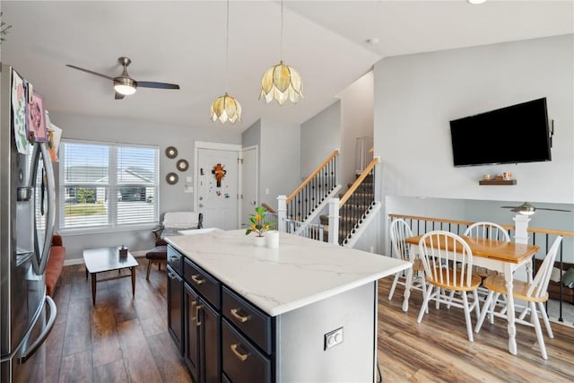 kitchen with dark wood-type flooring, a center island, hanging light fixtures, stainless steel fridge, and ceiling fan with notable chandelier