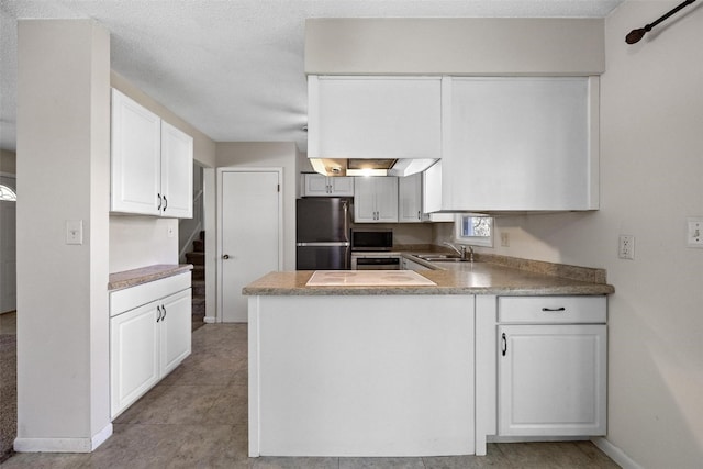 kitchen with white cabinets, stainless steel fridge, sink, kitchen peninsula, and a textured ceiling