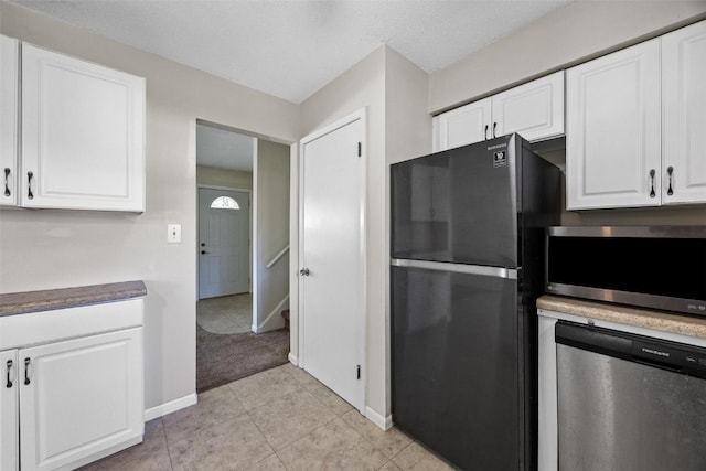 kitchen with a textured ceiling, stainless steel appliances, light tile patterned floors, and white cabinetry