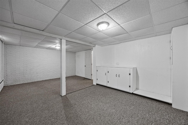 basement featuring a drop ceiling, carpet floors, and brick wall