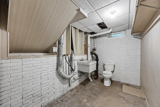 basement featuring a drop ceiling, brick wall, and sink