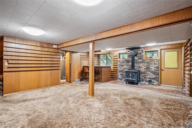 basement featuring carpet floors, wooden walls, and a wood stove